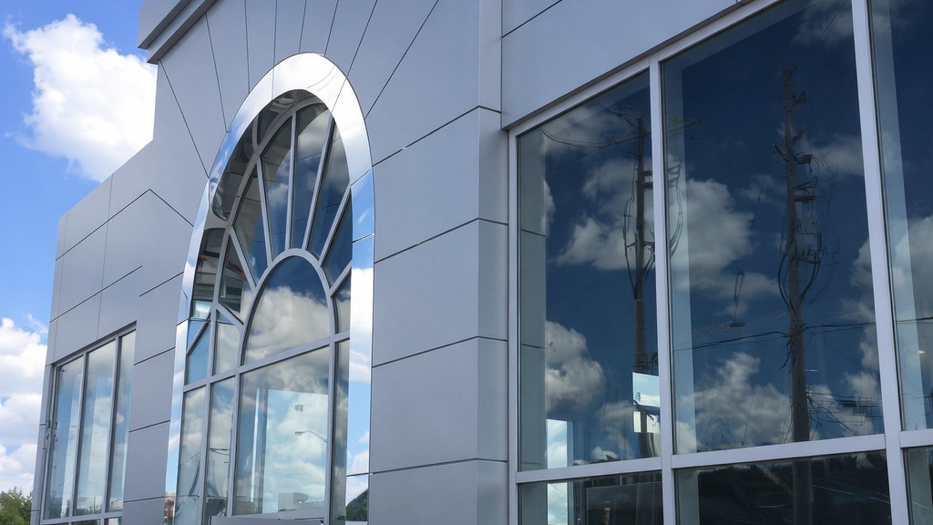 Finished dealership exterior with grey cladding, arched window, and blue sky reflections