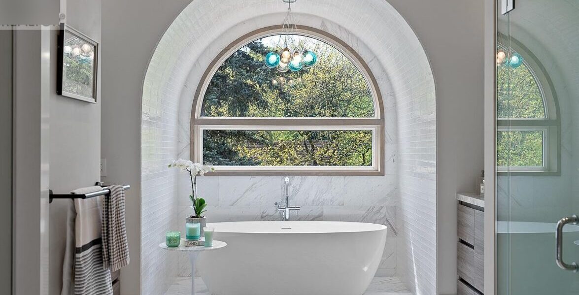 Freestanding soaker tub under marble arched alcove with natural light